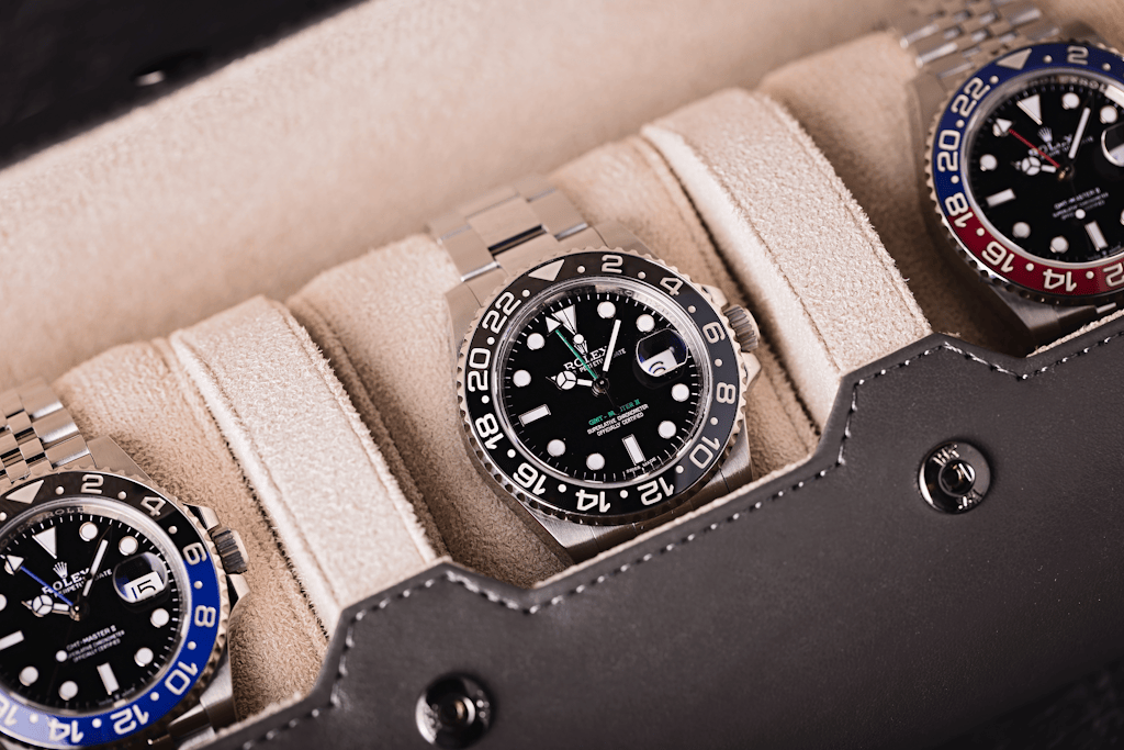 Three Rolex GMT-Master II watches with black dials and ceramic bezels displayed in a beige leather watch roll, featuring the black-and-blue ‘Batman’ and black-and-red ‘Pepsi’ bezel variants.